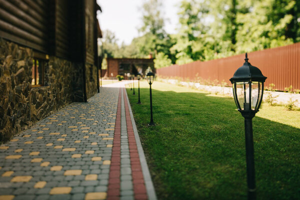 Уличные кованые металлические фонари на ухоженном коттедже с зеленой травой
 