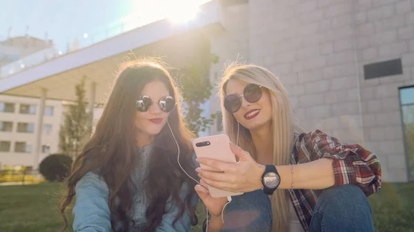 Dos chicas hipster atractivas usando un teléfono inteligente . —  Fotos de Stock