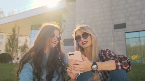 Dos chicas hipster atractivas usando un teléfono inteligente . — Foto de Stock