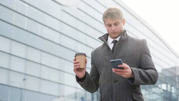 Handsome businessman in a city. Portrait of handsome business man using smartphone and drinking coffee in the city.