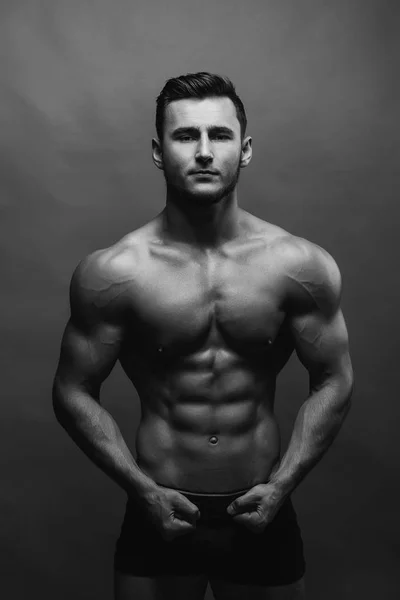 Black and white close up portrait of fitness athletic young boy showing muscles. Bodybuilding. Strong man posing on background.