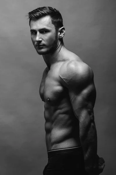 Black and white close up portrait of fitness athletic young boy showing muscles. Bodybuilding. Strong man posing on background.