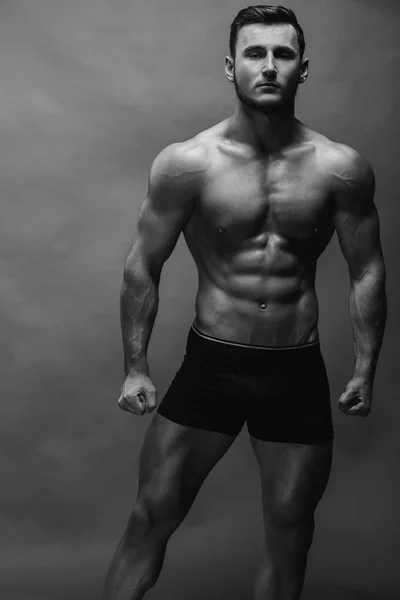 Black and white close up portrait of fitness athletic young boy showing muscles. Bodybuilding. Strong man posing on background.