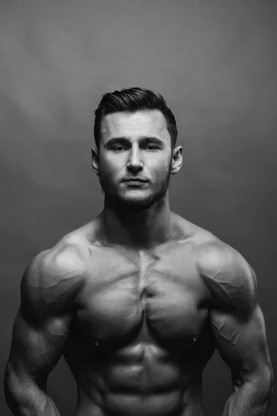 Black and white close up portrait of fitness athletic young boy showing muscles. Bodybuilding. Strong man posing on background.