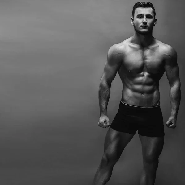 Black and white close up portrait of fitness athletic young boy showing muscles. Bodybuilding. Strong man posing on background.