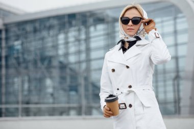 Çekici genç kadın kadar adımları açık havada yürürken kahve içme. Kahve fincanı Ofis Binası yakınındaki güzel kadınla. Açık havada yürüyüş güneş gözlüklü genç kadın.