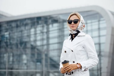 Çekici genç kadın kadar adımları açık havada yürürken kahve içme. Kahve fincanı Ofis Binası yakınındaki güzel kadınla. Açık havada yürüyüş güneş gözlüklü genç kadın.