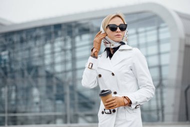 Çekici genç kadın kadar adımları açık havada yürürken kahve içme. Kahve fincanı Ofis Binası yakınındaki güzel kadınla. Açık havada yürüyüş güneş gözlüklü genç kadın.