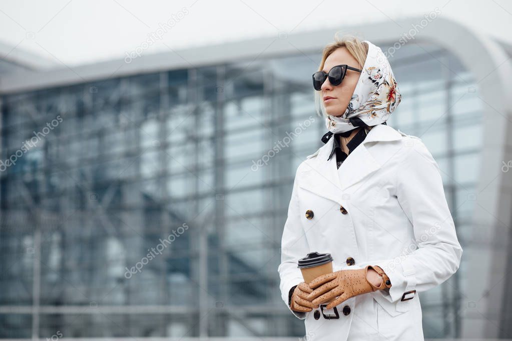 Attractive young woman drinking coffee while walking up the steps outdoors. Beautiful woman with coffee cup near office building.  Young woman in sunglasses walking outdoors.