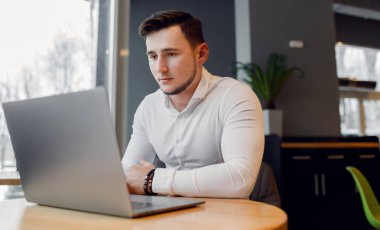 Genç adam bir kafe dükkanında dizüstü bilgisayar kullanarak.