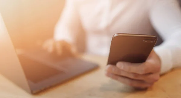 Mans handen met behulp van slimme telefoon en laptop in interieur. — Stockfoto