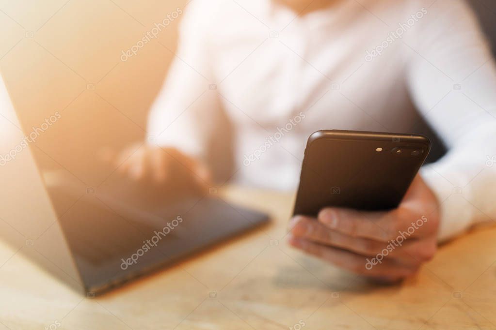 Mans hands using smart phone and laptop in interior.