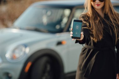 Car yakınındaki bir iş kadını. Arabanın yakınında Smartphone kullanan kadın. Araba sahipleri kavramı için cep telefonu uygulamaları.