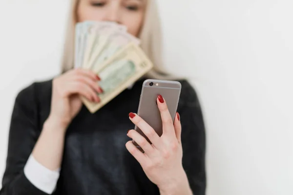Woman holding money and using smartphone.
