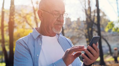 Aktif yaşlı adam parkta yürüyüş ve akıllı telefon kullanarak.