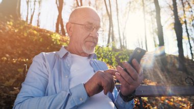 Aktif kıdemli adam parkta yürüyüş ve bankta parkta oturan akıllı telefon kullanarak.