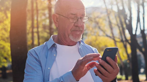 Active senior man walking in the park and using smartphone.