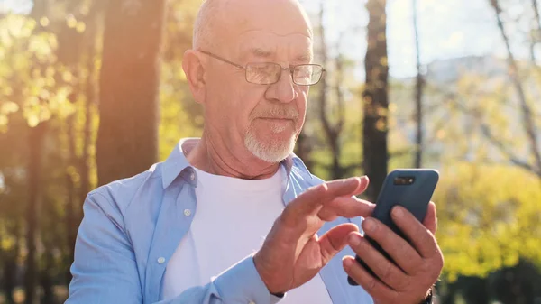 Active senior man walking in the park and using smartphone.
