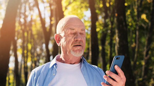 Active senior man walking in the park and using smartphone.