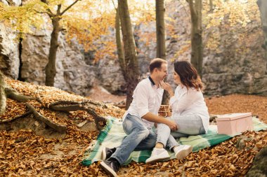 Romantik genç çift sonbahar parkında yürüyor. Parkta birlikte bir aile. Hamile çift.