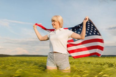 Buğday alanında Amerikan bayrağı tutan kadın. Amerika Patriots. Kız 4 Temmuz kutluyor.