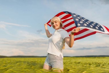 Buğday alanında Amerikan bayrağı tutan kadın. Amerika Patriots. Kız 4 Temmuz kutluyor.