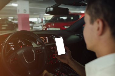 Arabada akıllı telefon tutan bir adam. Park yerindeki akıllı telefonun boş ekranı
