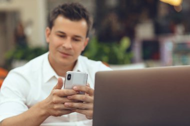 Kafede dizüstü bilgisayar ve akıllı telefon kullanan bir adam.