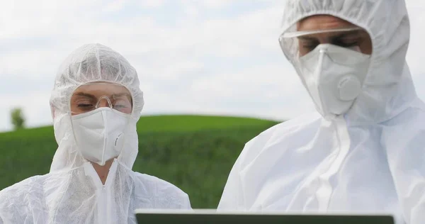 Close up of Caucasian female and male farmers researchers holding test tube with chemicals pesticides and laptop computer in green field. Biologists co-workers working and talking in wheat margin. — 스톡 사진