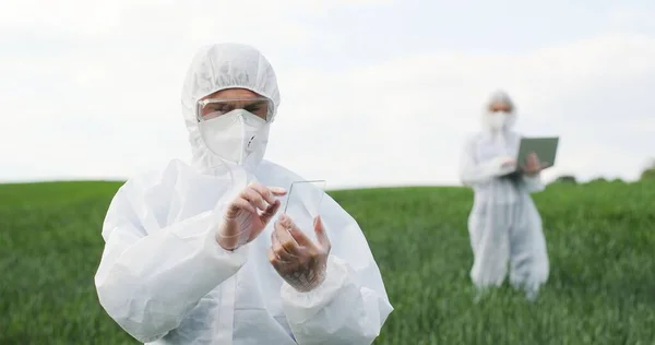 Glass futuistic smartphone in hands of male ecologist standing in green field in summer. Hi-tech technology of transparent device. Man in protective suit tapping on phone of future. Augmented reality. — 스톡 사진