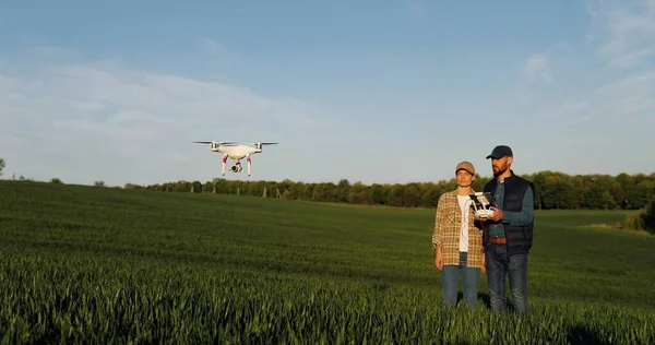 Caucasian happy couple of farmers standing in green wheat field and controlling of drone which flying above margin. Husband and wife using tablet device as controller. Technologies in agriculture. — Stockfoto