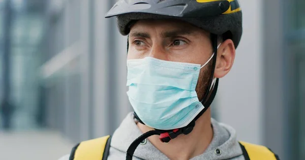 Close up portrait of male courier in medical mask and helmet for riding bike on bicycle delivering food.