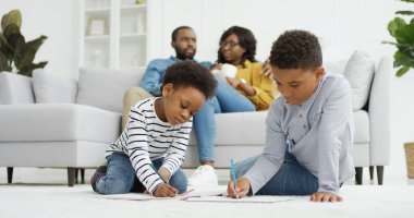 Mutlu Afro-Amerikan ailesi evde birlikte vakit geçiriyor. Ebeveynler oturma odasında kanepede birlikte dinlenirler, küçük çocuklar, erkek ve kız kardeşler evde resim çizerler..