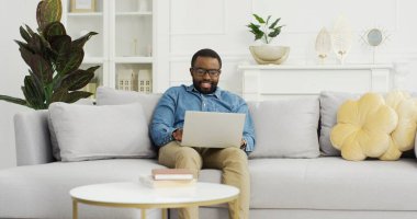 Evdeki koltukta dizüstü bilgisayar kullanan mutlu bir Afrikalı Amerikalı..