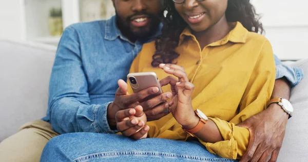 Glad afroamerikansk par sitter på soffan med hjälp av smartphone — Stockfoto