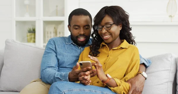 Glad afroamerikansk par sitter på soffan med hjälp av smartphone — Stockfoto