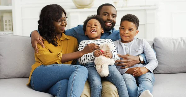自宅のソファの上に小さな子供とアフリカ系アメリカ人の両親の肖像画。7月4日の家族の祝日、愛国の休日. — ストック写真