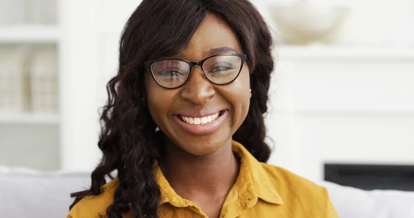 坐在家里的沙发上，用眼镜把快乐的非裔美国女人的肖像合上. — 图库照片