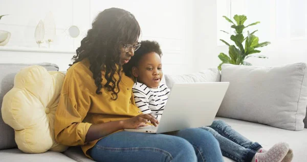 Portret van Afrikaanse Amerikaanse moeder en schattig dochtertje kijken iets op laptop thuis. — Stockfoto