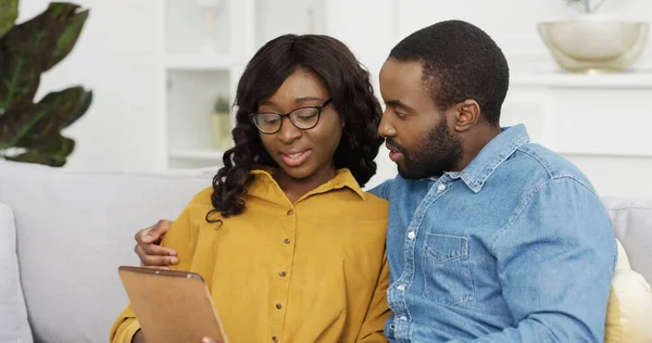 Šťastný africký americký pár manžel a manželka sedí na pohovce pomocí tabletu a kreditní karty pro on-line nakupování doma. — Stock fotografie