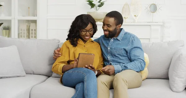 Šťastný africký americký pár manžel a manželka sedí na pohovce pomocí tabletu a kreditní karty pro on-line nakupování doma. — Stock fotografie