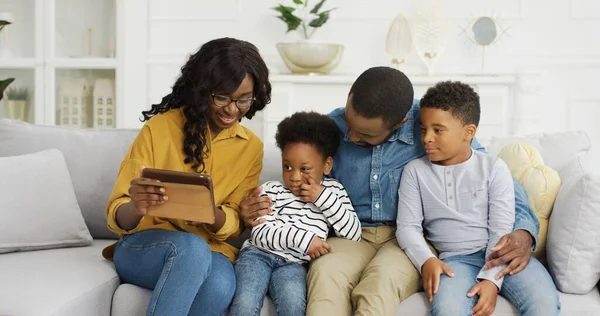 Happy Afro-Amerikaanse familie zitten op de bank met behulp van tablet thuis. — Stockfoto