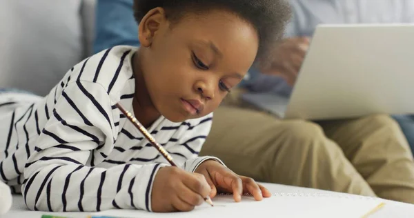 Portrait de petite fille afro-américaine dessinant sur fond de son père avec son frère à l'aide d'un ordinateur portable. — Photo