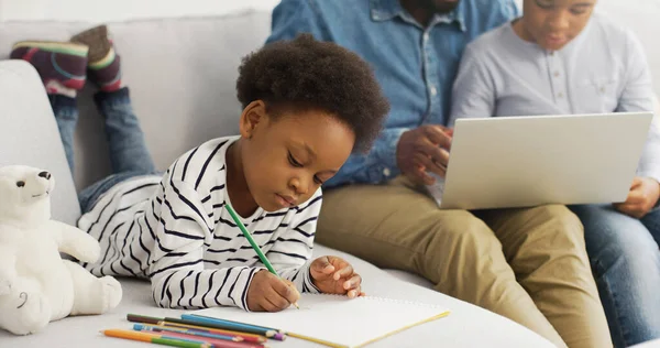 Afro-Amerikaanse vader met behulp van laptop plezier te spelen met kinderen zitten op de bank. — Stockfoto