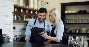 Neşeli güzel garson ve garson barda durup tablet bilgisayardan video izleyip sohbet ediyorlar..