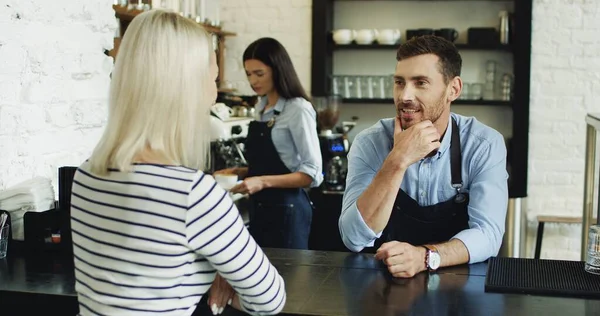 Snygg servitör pratar med söt blond klient i baren, medan servitris serverar sitt kaffe. — Stockfoto