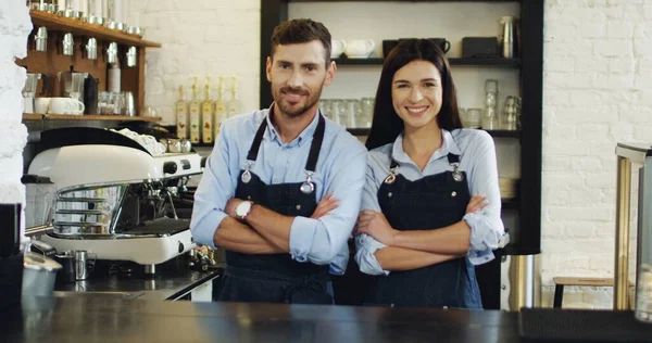 Portraitaufnahme der kaukasischen attraktiven Kellnerin und Kellnerin, die Rücken an Rücken an der Bar steht, sich dann umdreht und in die Kamera lächelt. Caféarbeiter. — Stockfoto