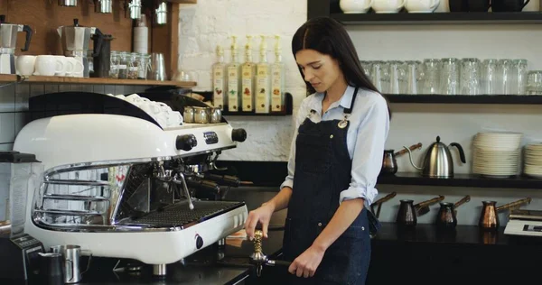 Zdjęcie portretowe ślicznej uśmiechniętej kelnerki przygotowującej kawę na ekspresie do kawy i patrzącej w kamerę. — Zdjęcie stockowe