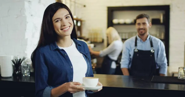 Barmen caucásico guapo sirviendo café a la hermosa morena en el bar, luego se gira y sonríe a la cámara . —  Fotos de Stock