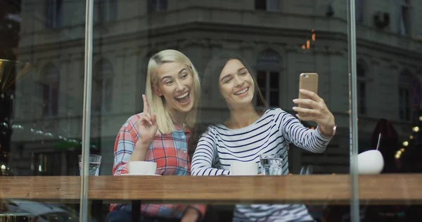 Hermosas dos mujeres posando y tomando buenas fotos selfie en la cámara del teléfono inteligente mientras se sienta con café en la cafetería . —  Fotos de Stock